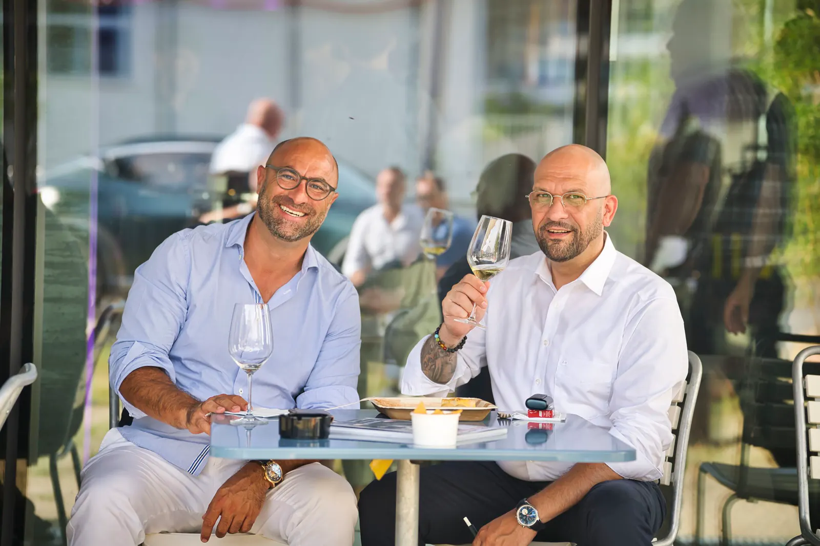 Zwei Gäste am Tisch, einer prostet mit dem Weinglas zu
