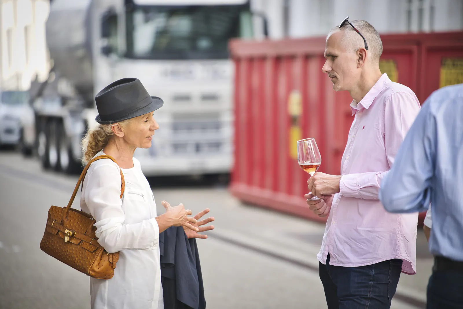 Zwei Gäste des BASELWIRTSCHAFT Networking Events im Gespräch, eine Frau mit Hut spricht, ein Mann hört zu